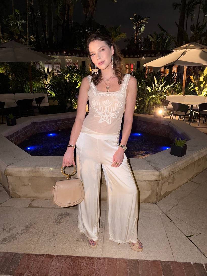 White embroidered top and satin trousers by a lit fountain at night