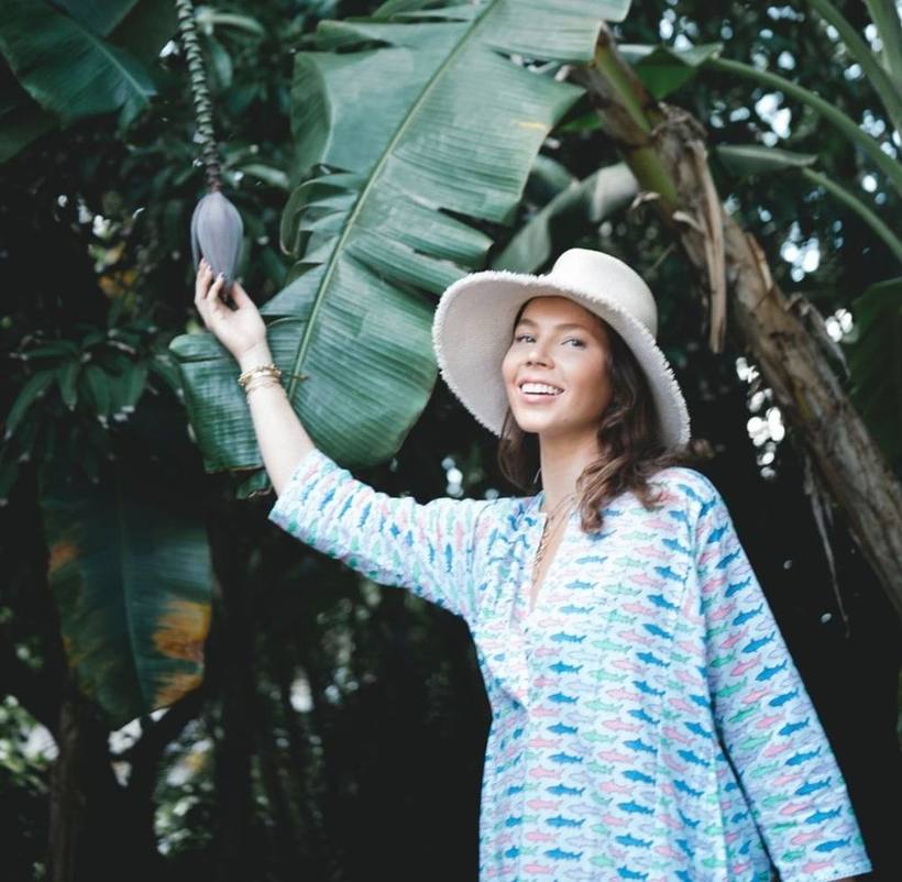 Smiling under banana leaves in a sun hat and printed tunic