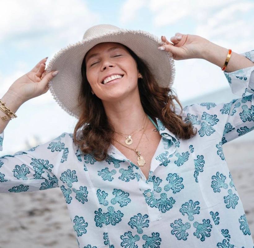 Laughing on the beach, both hands on a sun hat